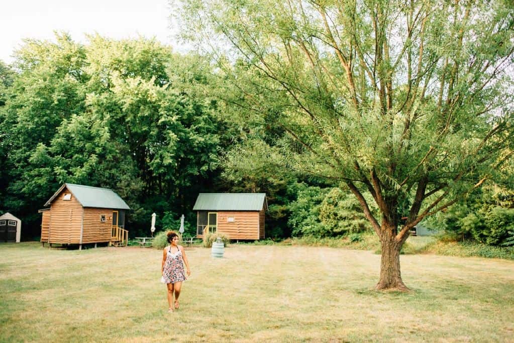 Two cabins in a forest clearing with a girl in a dress walking