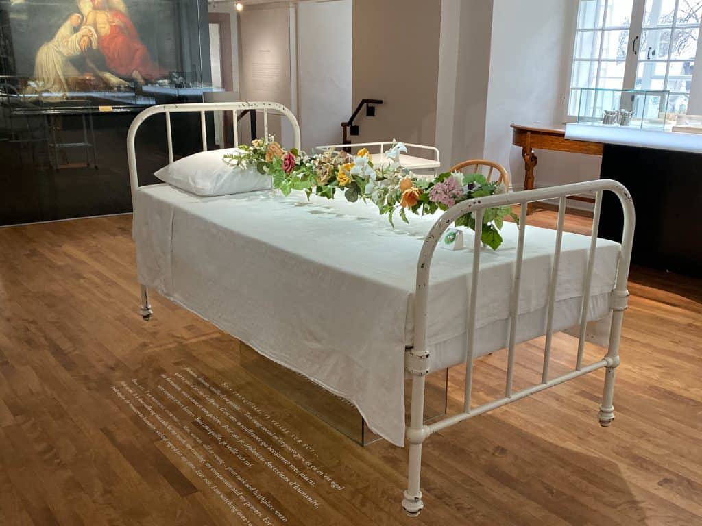 Hospital bed with flowers above - museum exhibit at Le Monastere des Augustines