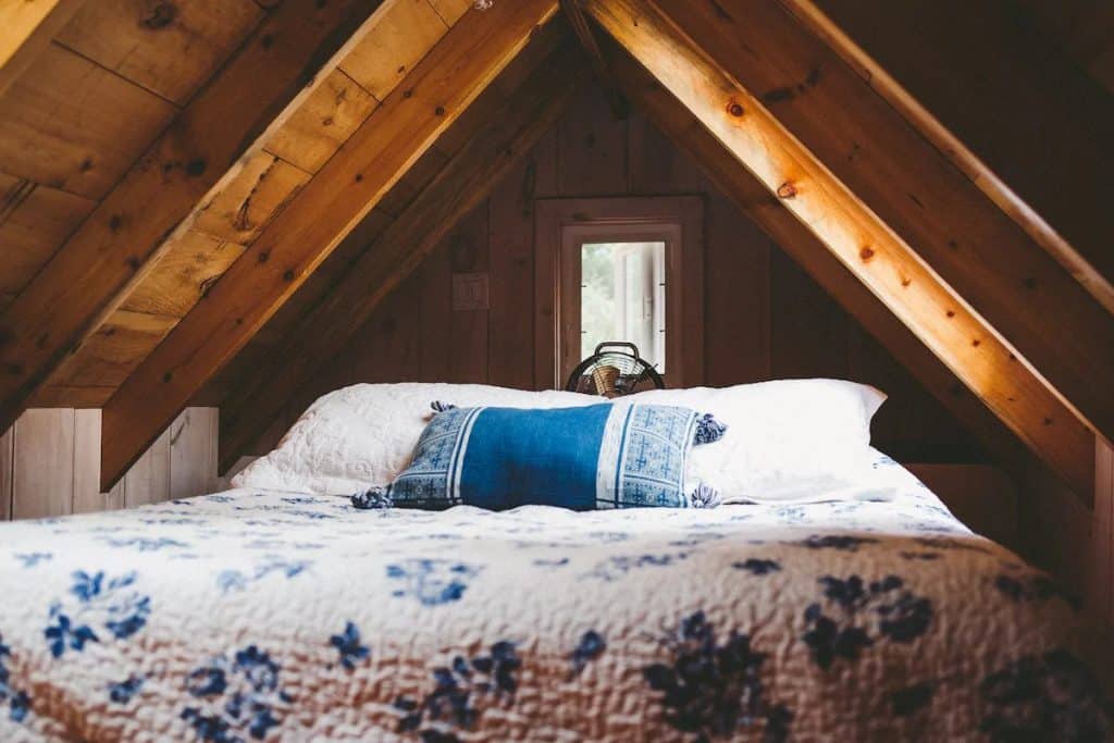 Mattress covered in blue and white quilt in an A-frame cabin loft.