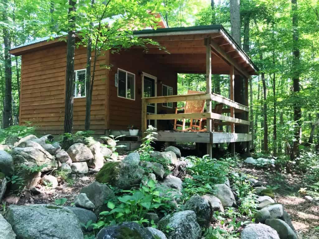 A tiny house with a roofed porch in the woods.