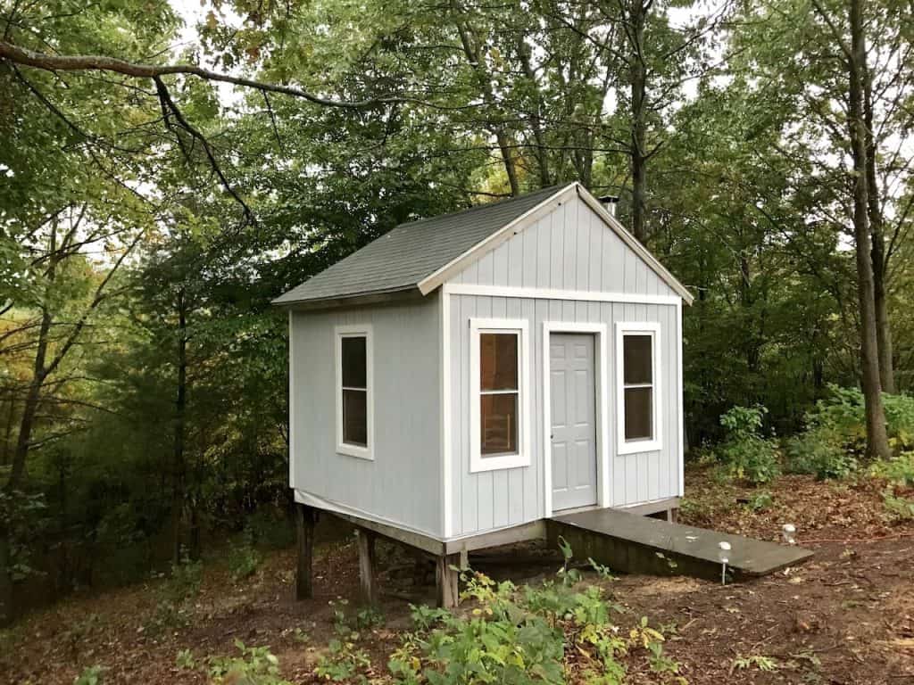 A pale gray tiny house in a forest.