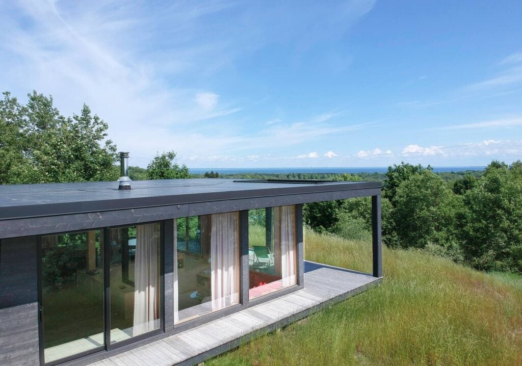 Modern cabin with numerous glass windows overlooking the forest below.