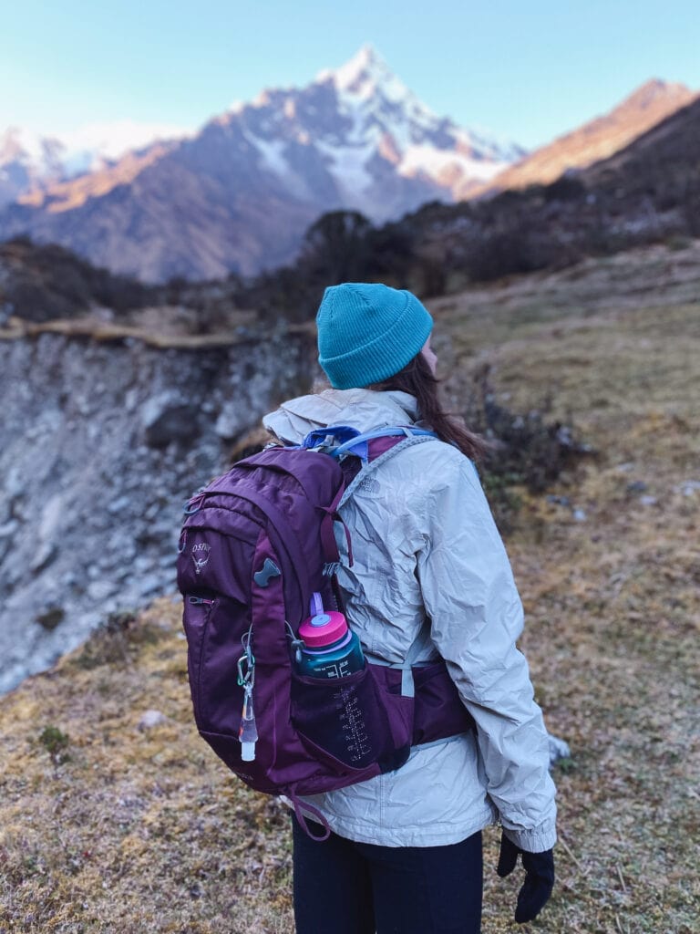 Girl with purple backpack and blue hat looks toward the mountains along the salkantay trek to Machu Picchu