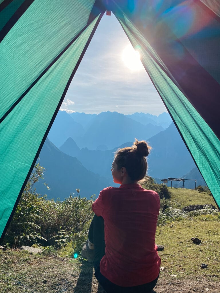 Sarah sitting in the opening of a green tent at sunrise along the salkantay trek