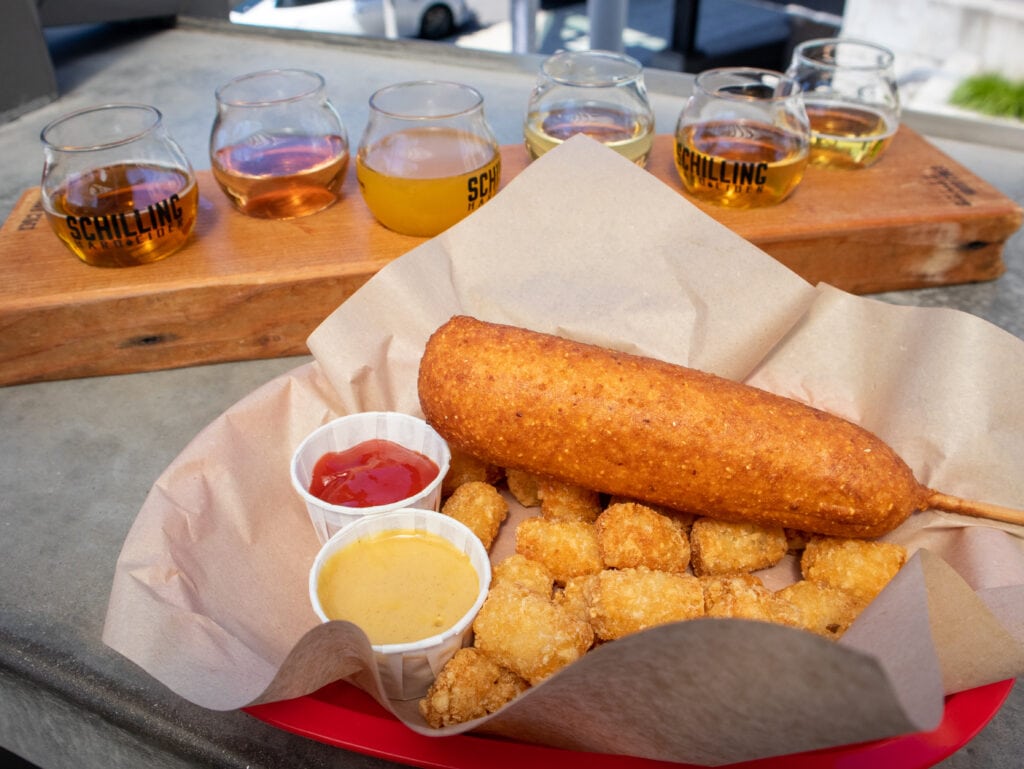 gluten free corn dog and tater tots with gluten free cider flight in the background
