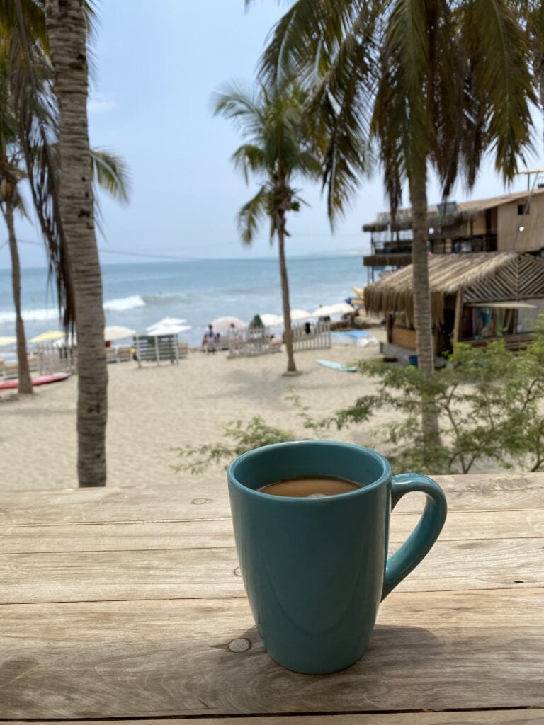 Coffee on a deck in front of an ocean beach with palm trees in Mancora Peru.