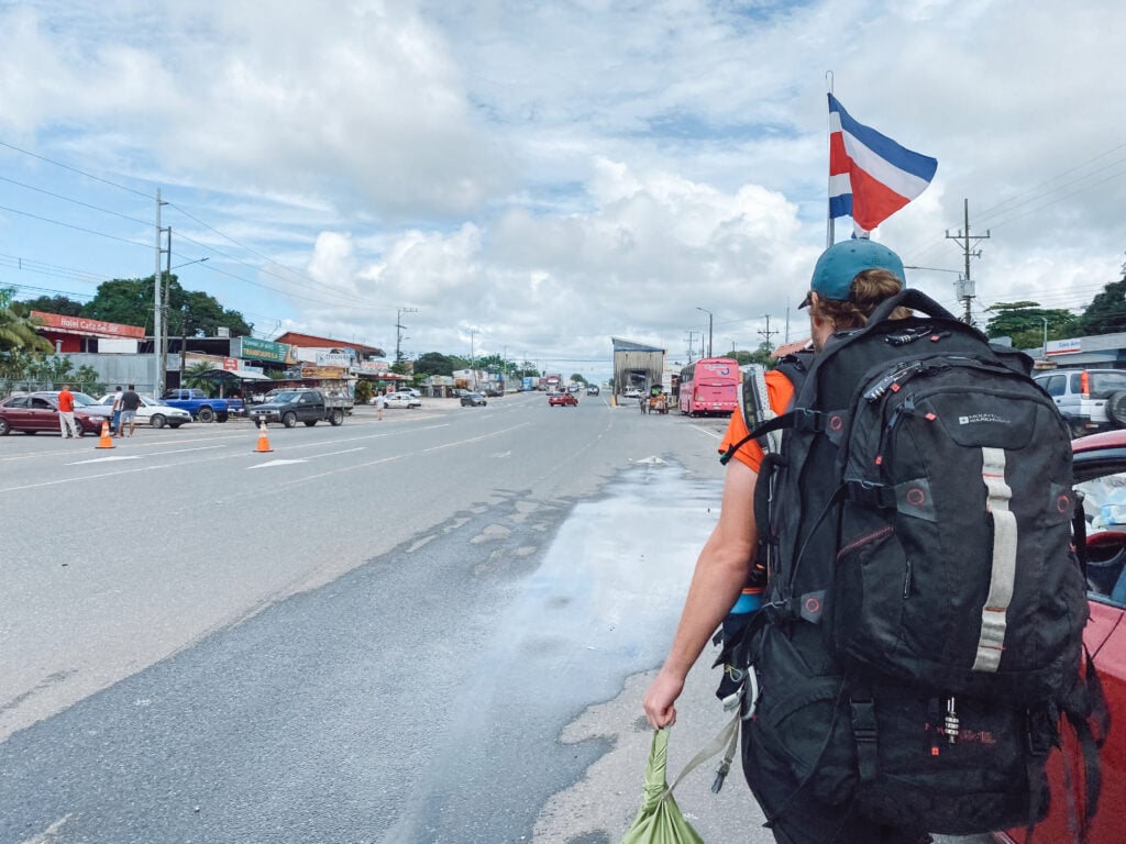 dan with big black backpack and the costa rican flag walking in no man's land at the panama to costa rica border crossing