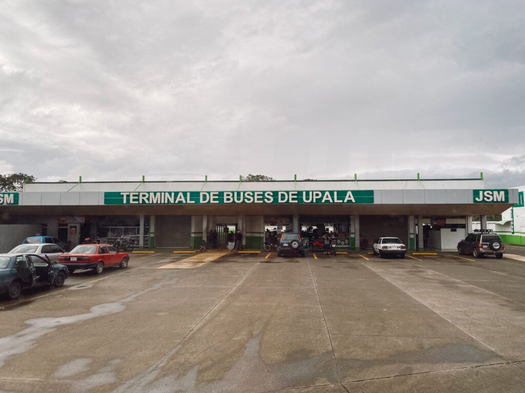 A short gray building with a green sign that says terminal de buses de upala.