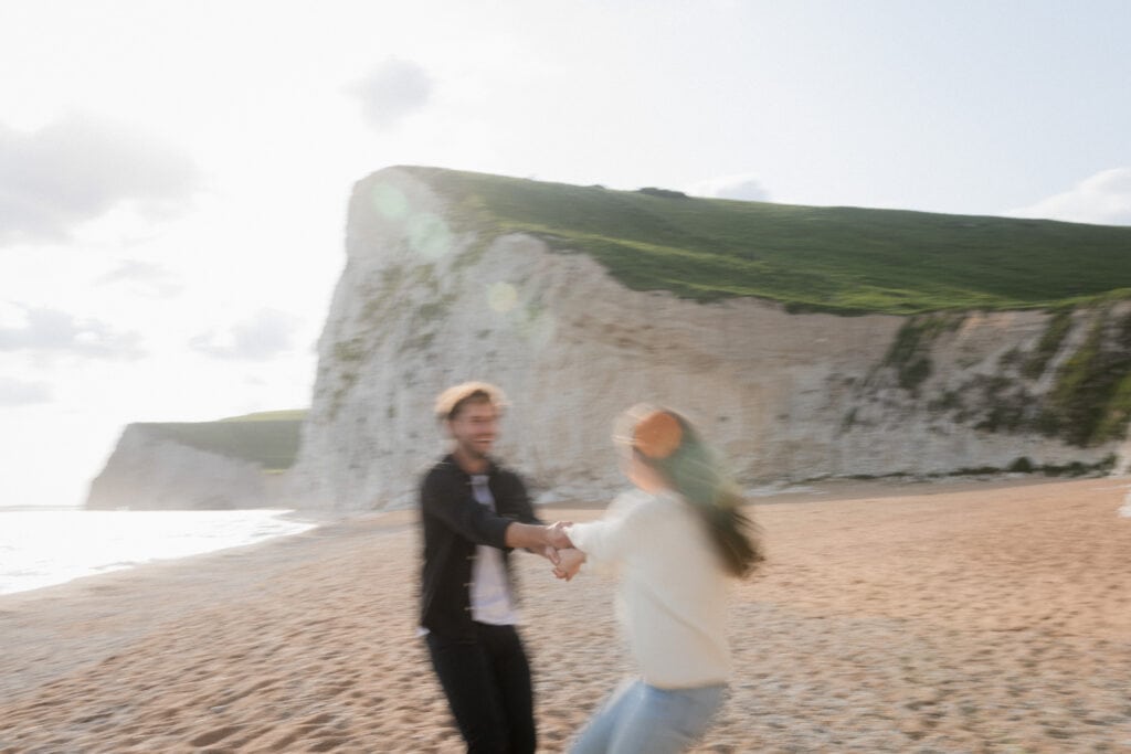 Sarah and Dan hold hands and spin in circle on the beach