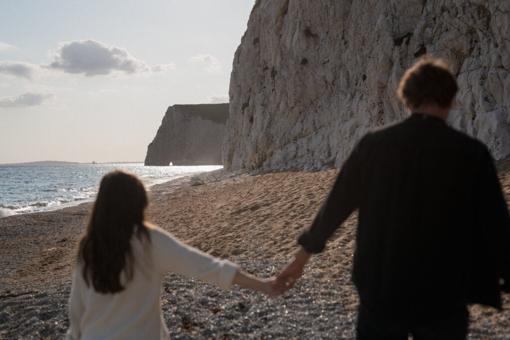 Sarah and Dan walk away holding hands on beach
