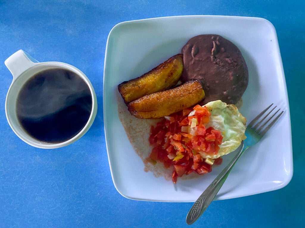 A typical breakfast in El Salvador of plantains, tomato salsa, eggs, and refried beans with coffee.