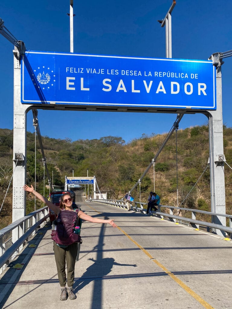 Sarah standing on a bridge with her arms out under the exit el salvador sign.