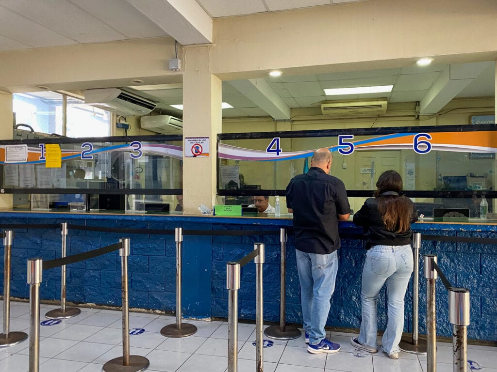 A blue brick wall with numbered desks of immigration officers and two people having their passports checked.