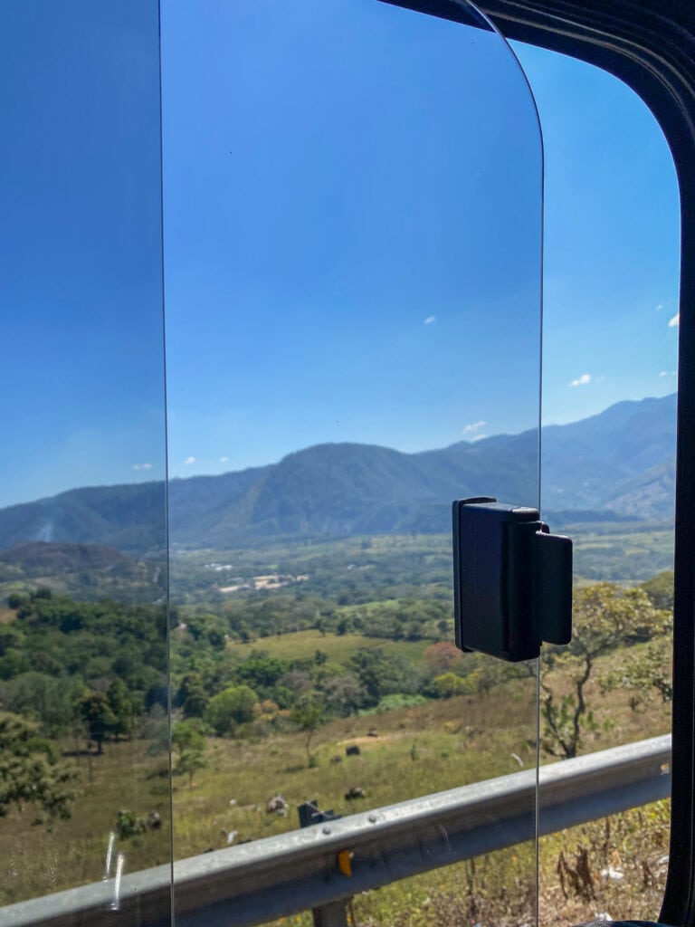 Views of green hills out a bus window.