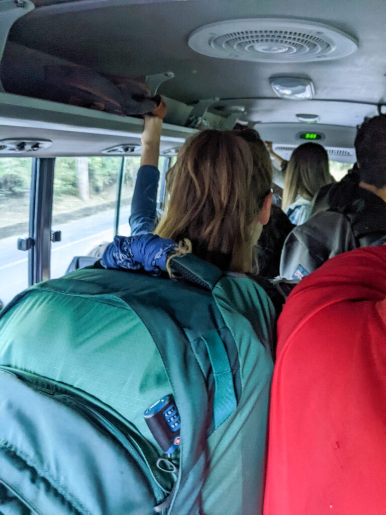 Sarah standing packed in a group of people on a bus wearing a big green backpack.