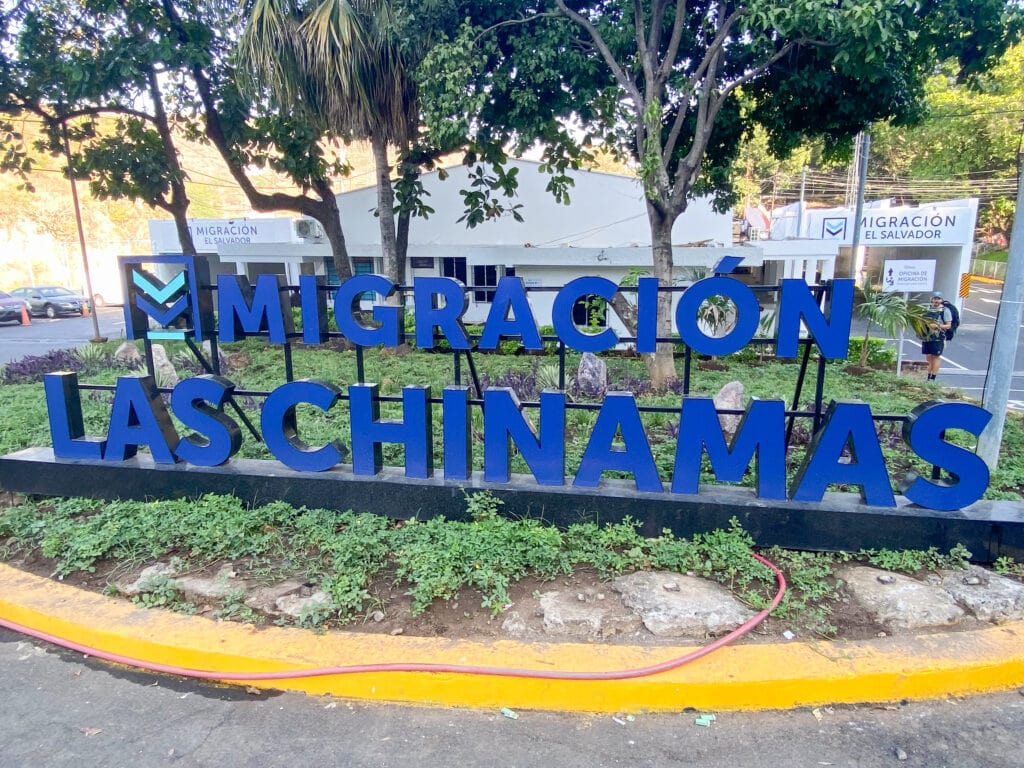 A blue sign that says Migracion Las Chinimas in front of the white immigration building.