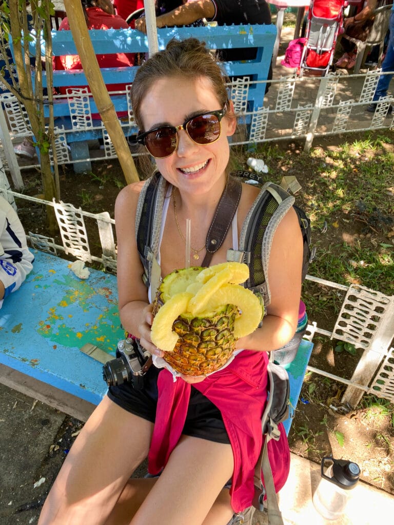 Sarah smiling at camera while sitting pineapple juice out of a pineapple.