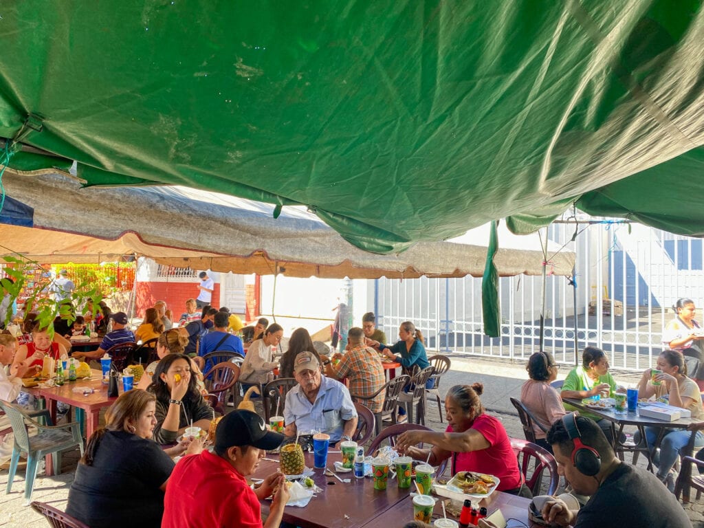 Salvadoreans eating at the Juayua food festival under a green tent.