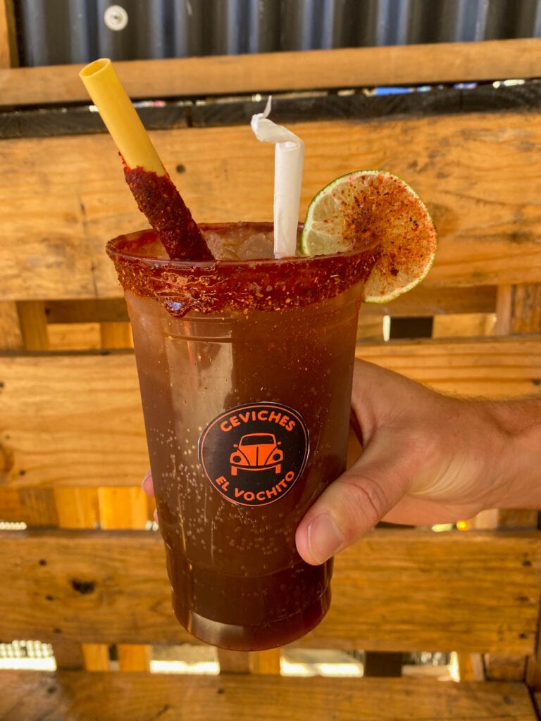 A plastic cup with michelada in it and a sticker that says ceviches el vochito.