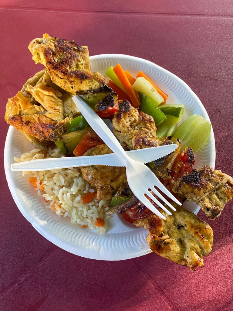 A kebab platter at the Juayua food festival on a styrofoam plate on a red plastic table.