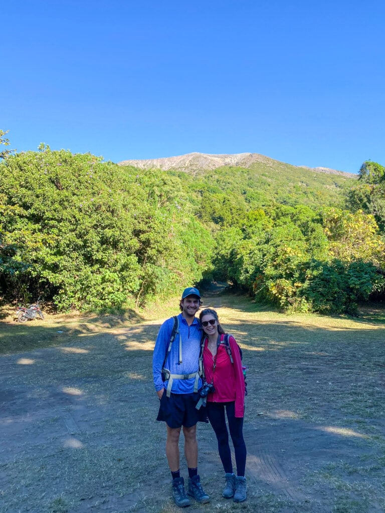 Dan and Sarah stand smiling in front of the path up Santa Ana Volcano
