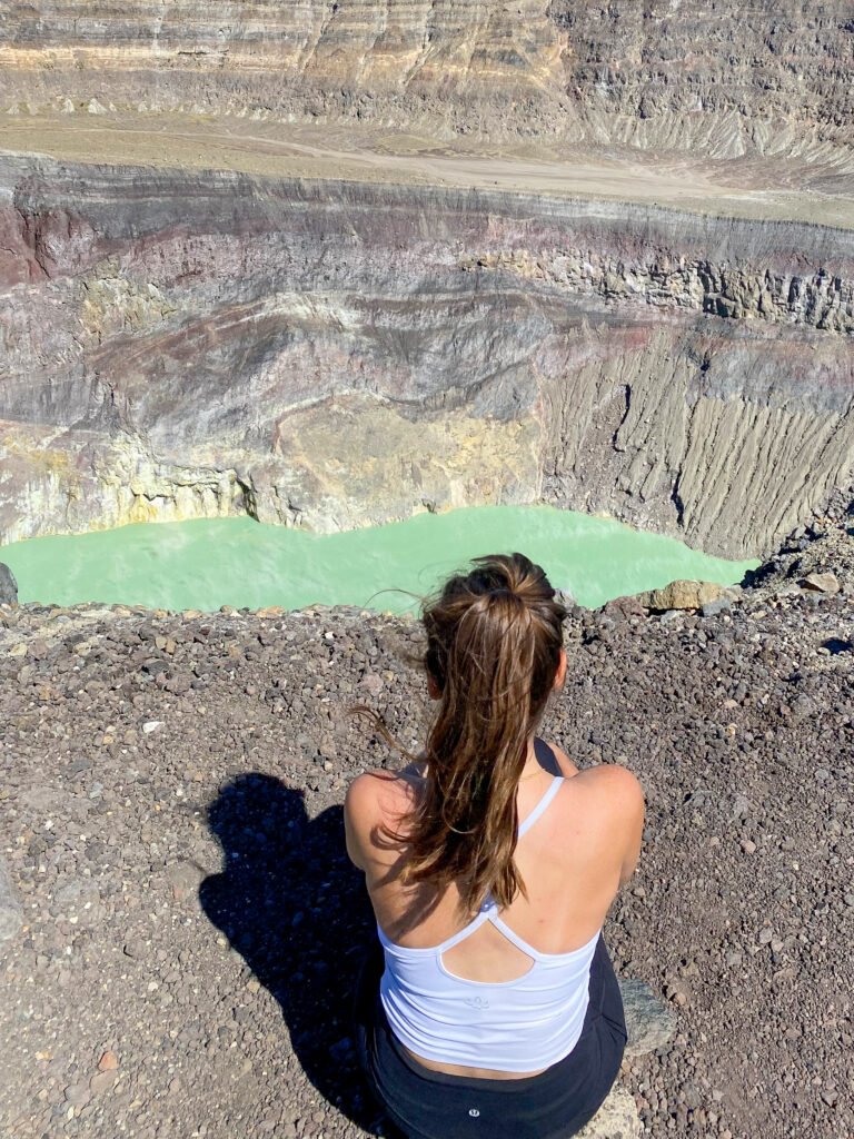 Sarah sitting on the ground after hiking Santa Ana Volcano and looking out at the crater lake