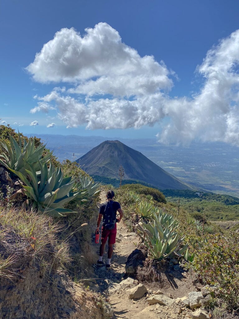 Man walking down path with Izalco Volcano in the distance.
