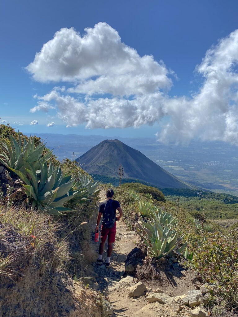 Man walking down path with Izalco Volcano in the distance.