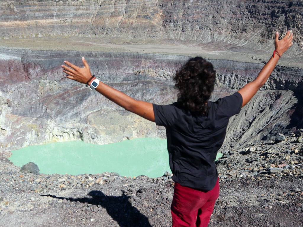 Man with red shorts holds out his arms in front of Santa Ana Volcano crater.