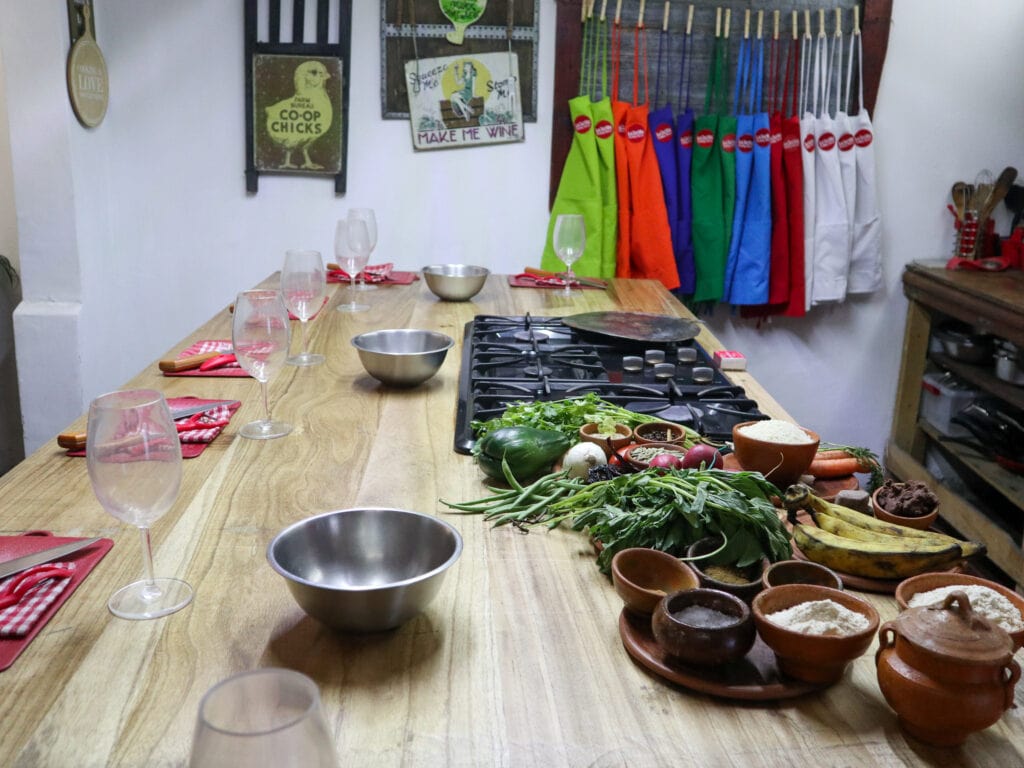 A kitchen with a wooden table, place settings with wine glasses, and colorful aprons in the background.