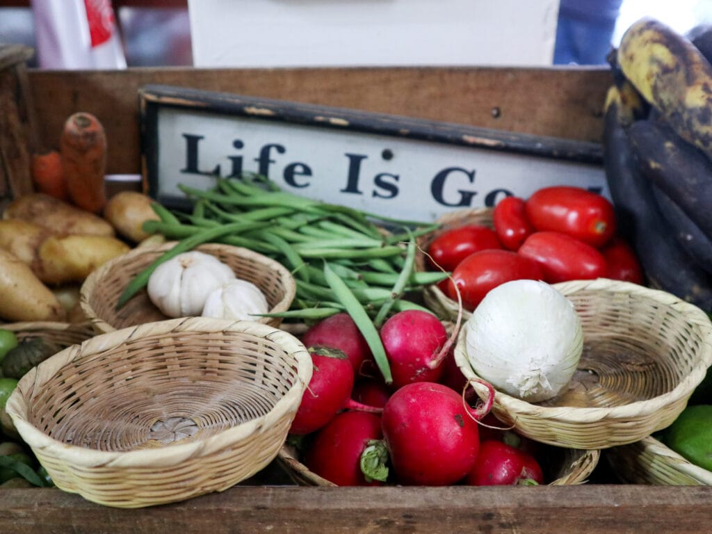 A wooden basket full of vegetables including tomatoes garlic and radish, with a sign that says life is good.