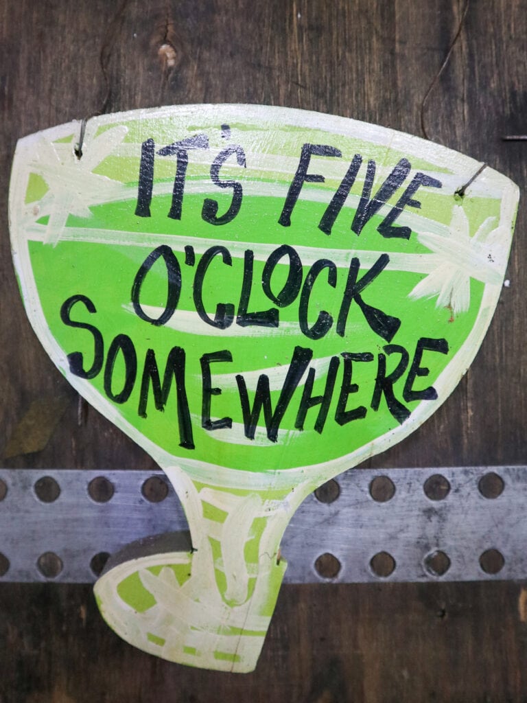 A sign that says it's five o'clock somewhere, painted inside a green cocktail-glass shaped sign.