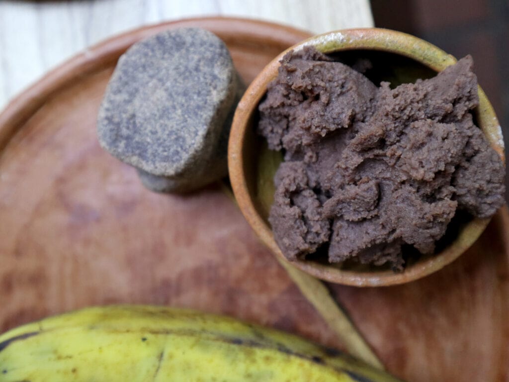 An aerial view of a tray with a slice of chocolate, plantain, and bowl of refried beans.