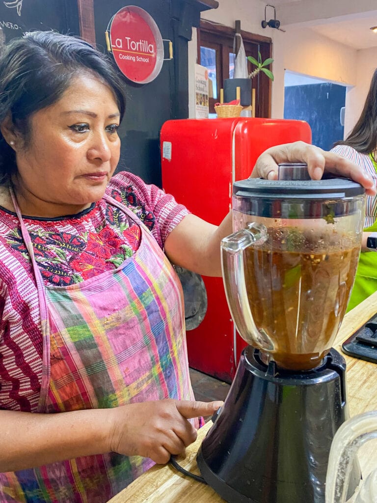 Sonia, a Guatemalan woman, wears a colorful pink plaid apron and works a blender.