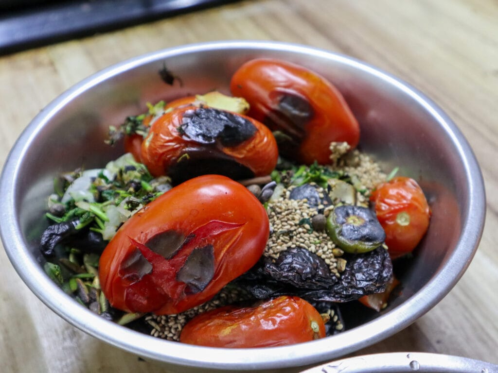 A metal bowl with roastd tomato, sesame seeds, and chiles in it.