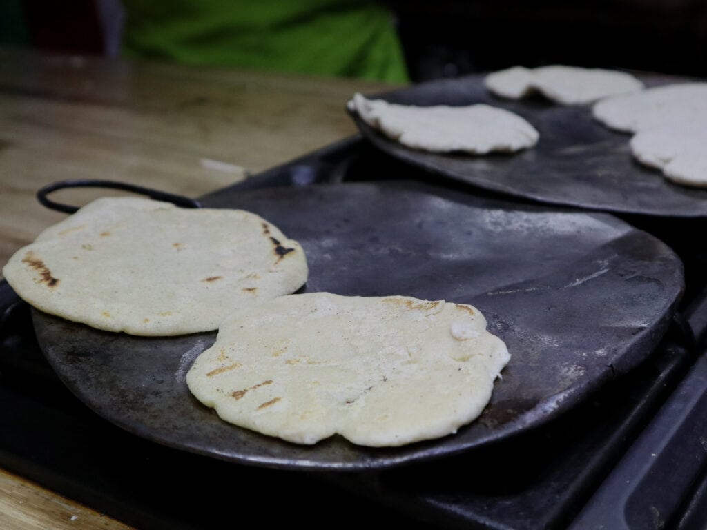 Corn tortillas cooking on a flat pan.