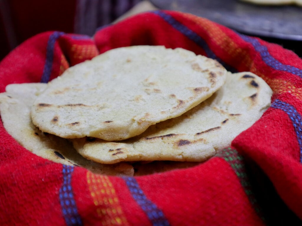 Corn tortillas in a basket with a red cloth.