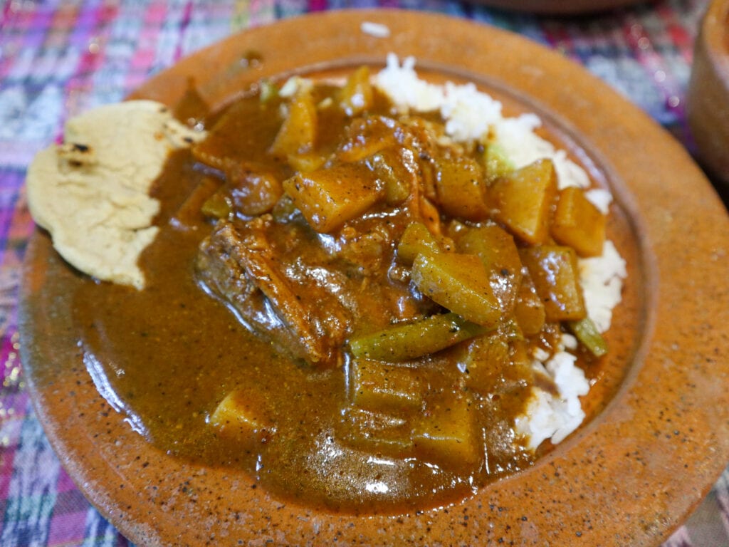 A clay plate with pepian dish, Guatemala's national dish, accompanied by rice and corn tortilla.
