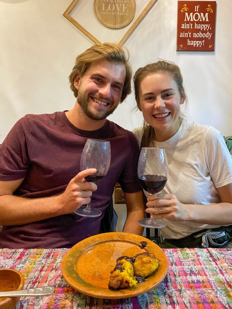 Dan and Sarah each hold a glass of wine and smile at the camera.