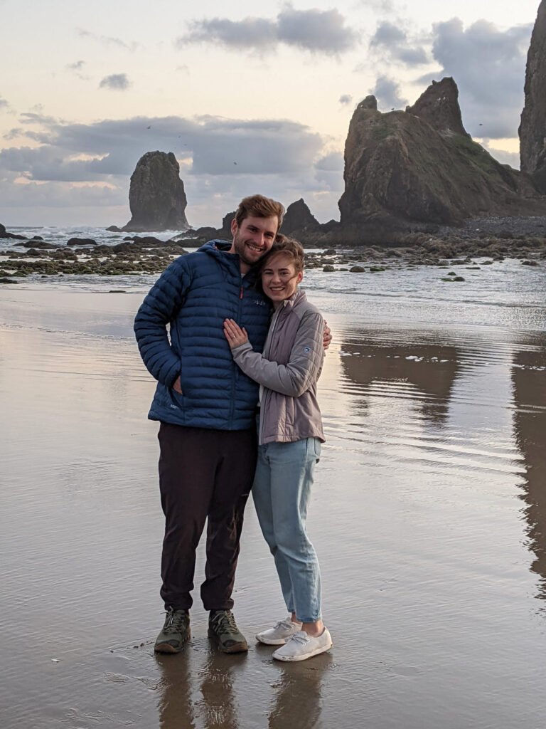 Sarah and Dan smiling on Cannon Beach at sunset on their engagement