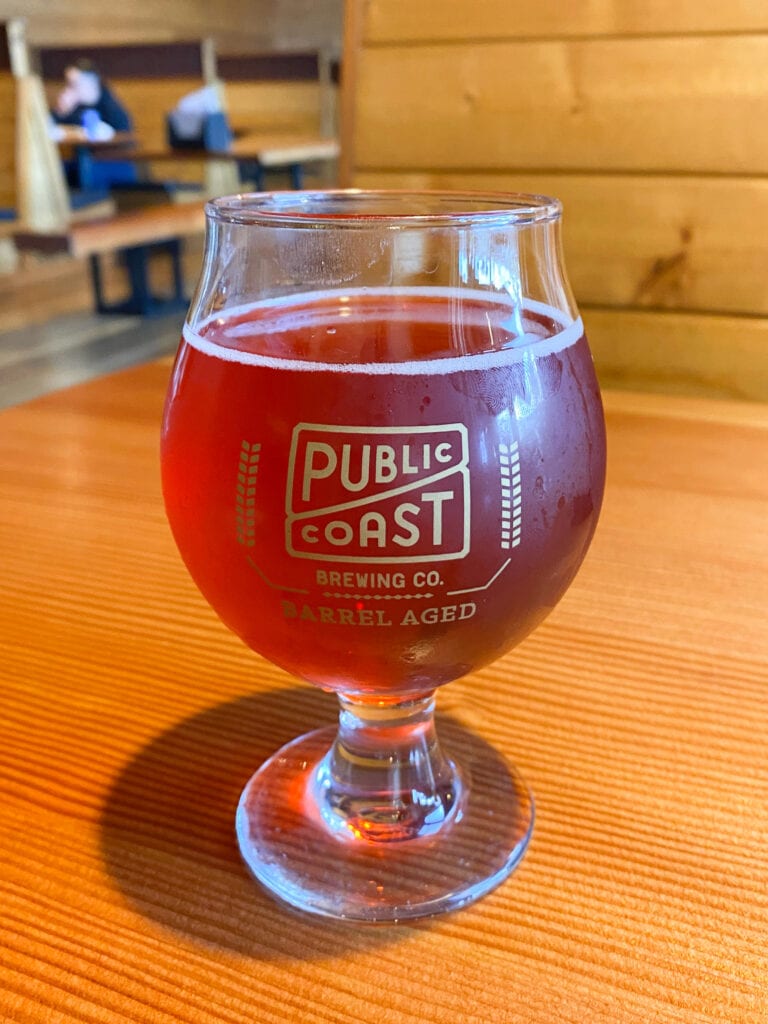 A dark brown cider in a glass that says Public Coast Brewing Company
