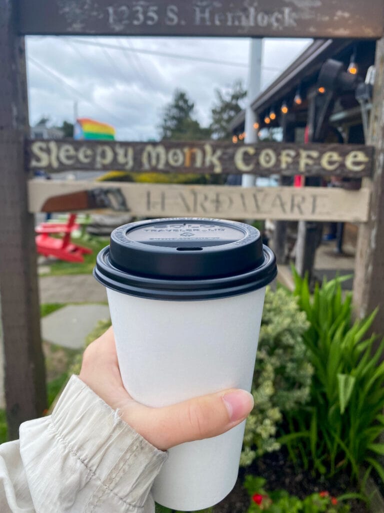 Coffee to go cup in front of Sleepy Monk Coffee Sign