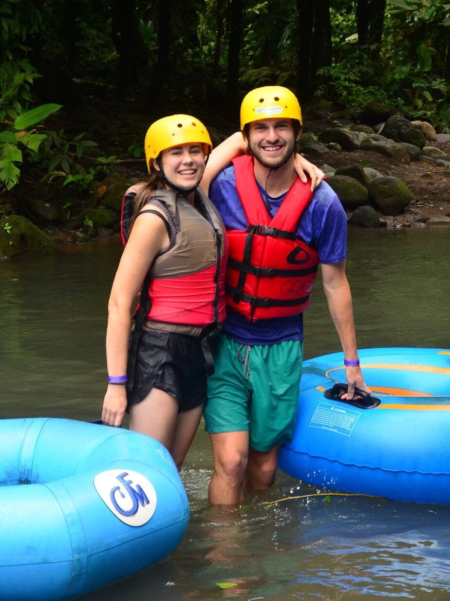 sarah and dan wearing helmets and standing in a river with inner tubes.