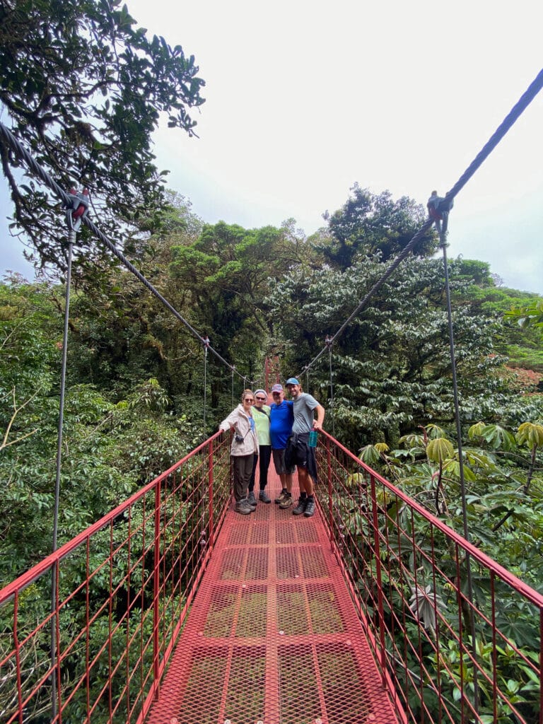 sarah, her mom and dad, and dan stand on a red hanging bridge in monteverde costa rica