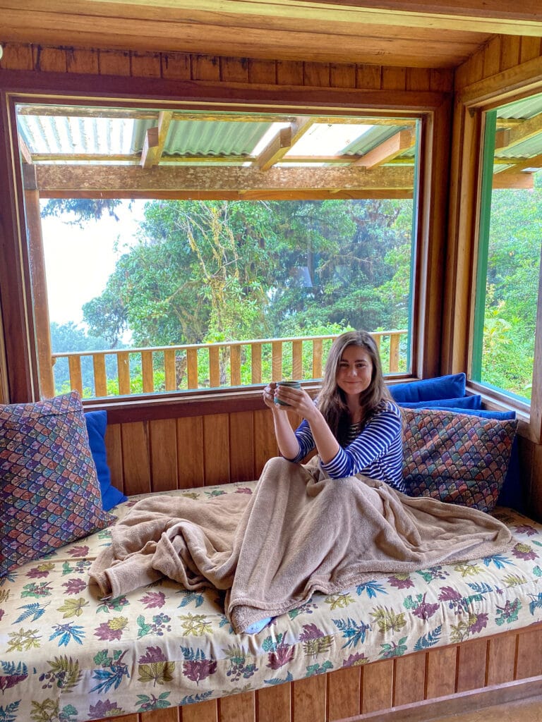 sarah sitting in a window seat with a blanket and cup of coffee