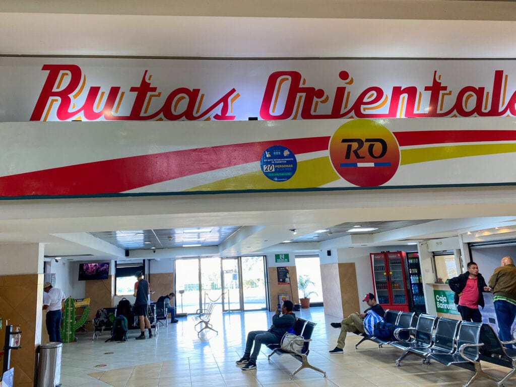 A seating area in a bus terminal under a red and white sign that says Rutas Orientales.