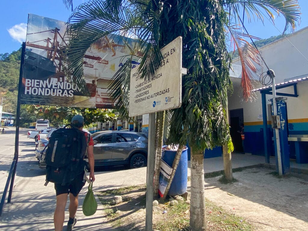 Backpacker traveler walking under sign that says Bienvenido a Honduras.