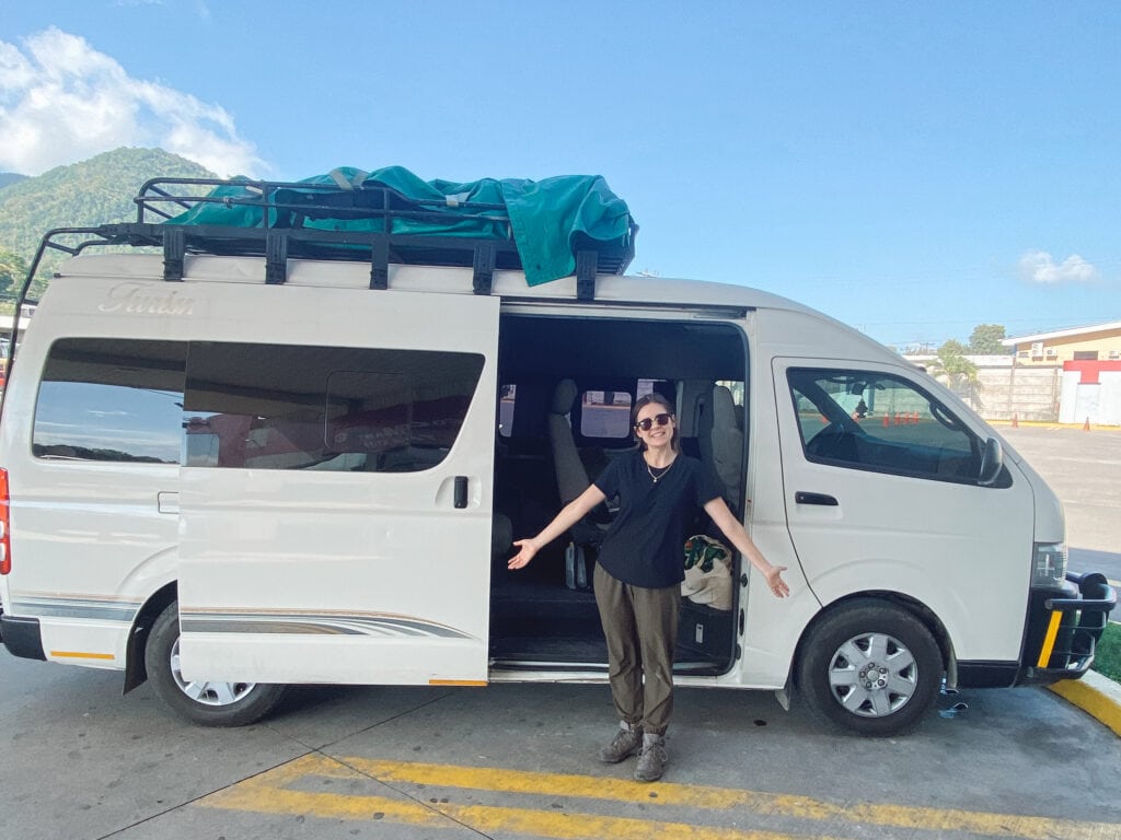 Sarah standing in front of a white shuttle truck with her arms held out.