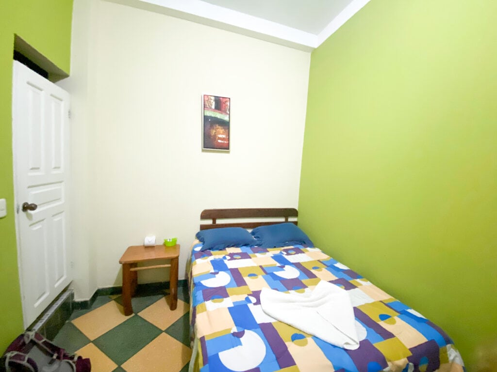 A green hotel room with a double bed with a geometric pattern duvet in Rio Dulce Guatemala.