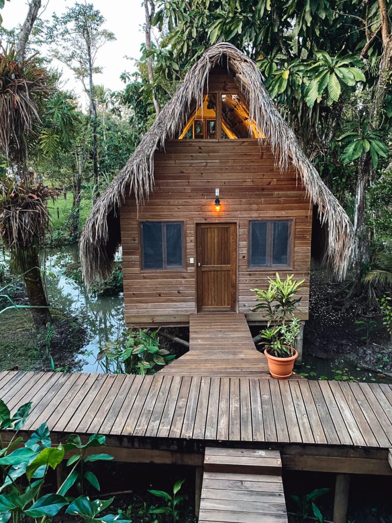 A wooden A frame cabin with a thatch roof built over a river
